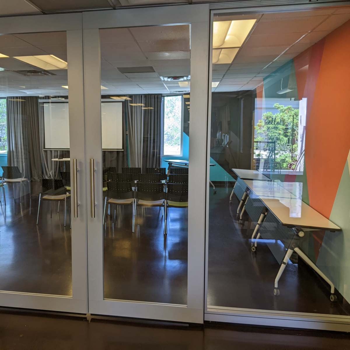 A modern conference room with glass doors, featuring rows of black chairs and tables arranged for a meeting.