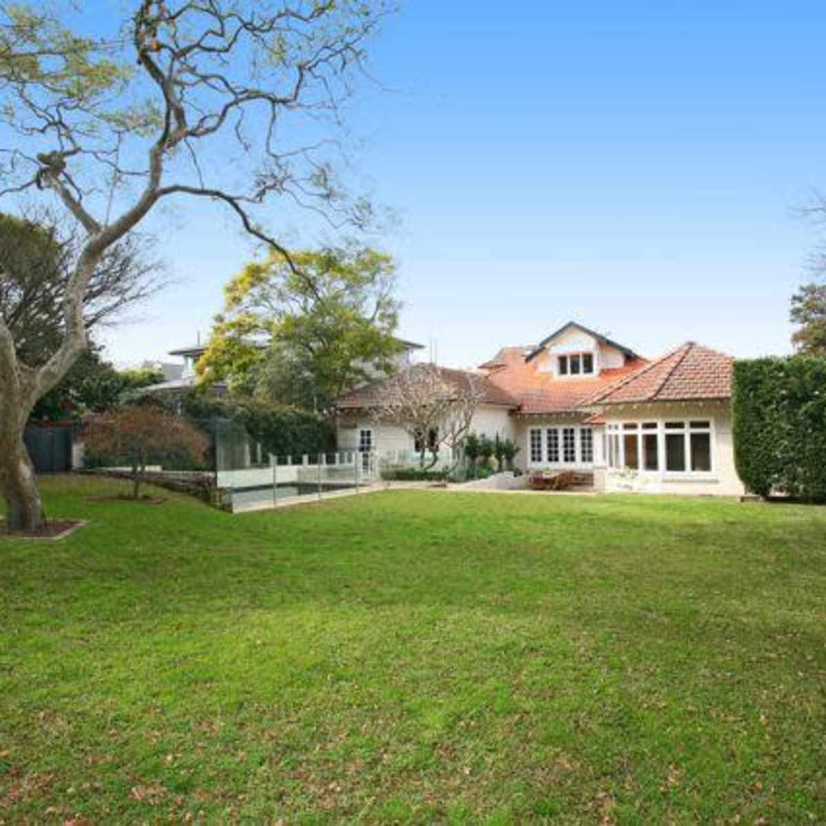 A spacious backyard features a well-maintained lawn with a tree and a house in the background.