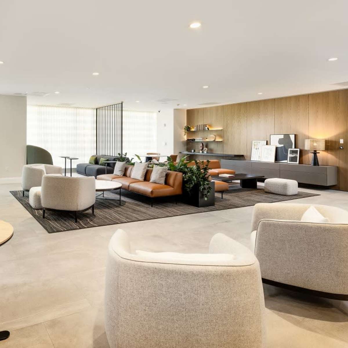 A modern lounge area featuring green and brown seating, small tables, and a variety of plants.