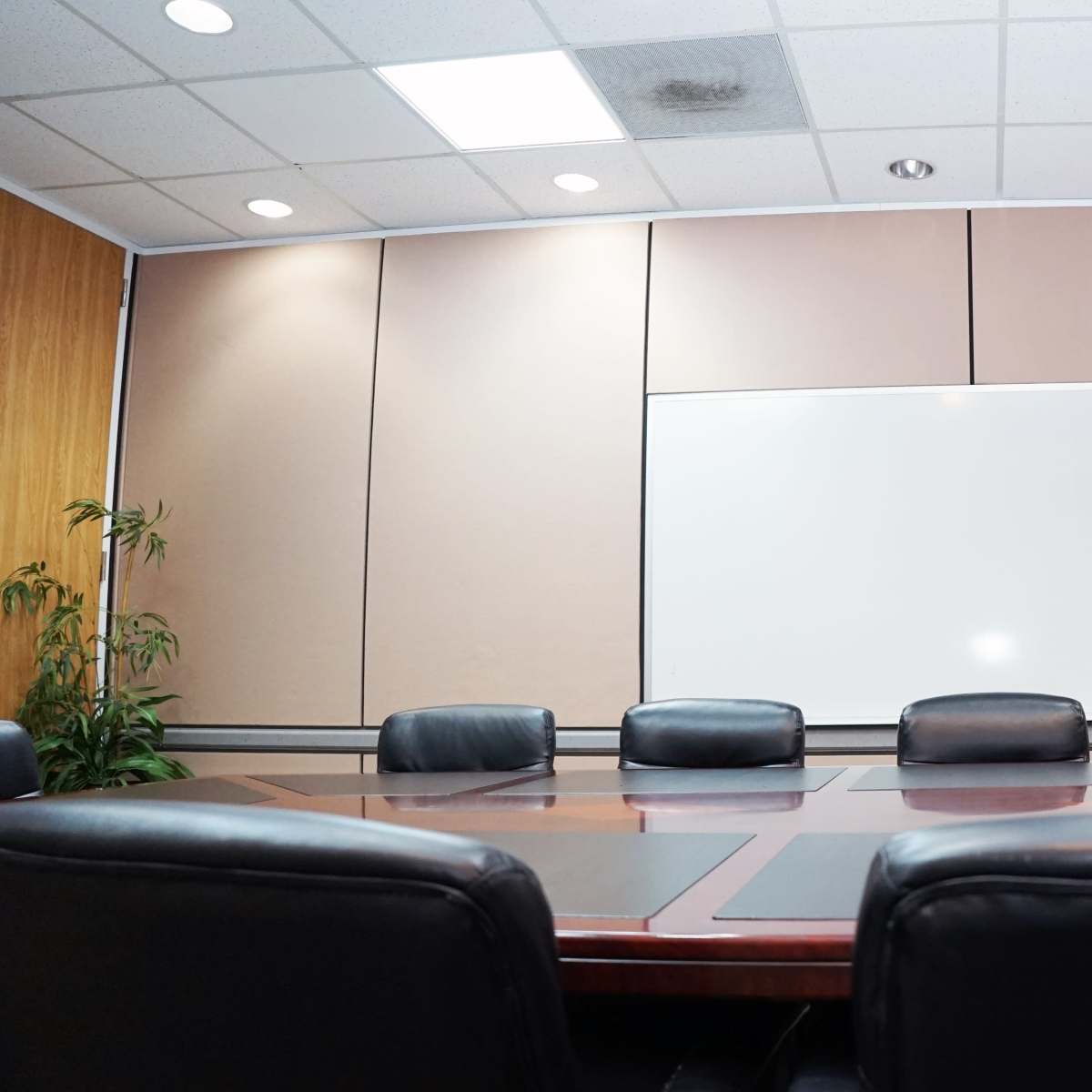 A conference room features a long wooden table surrounded by black leather chairs, with a blank whiteboard on the wall.