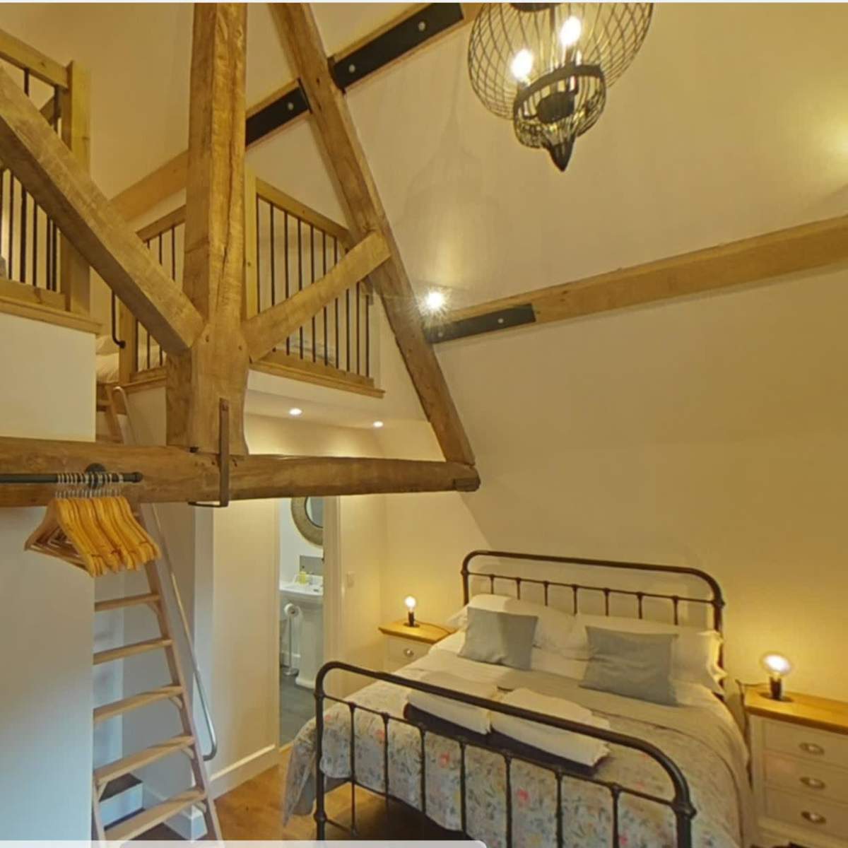 A cozy room with a lofted sleeping area, exposed wooden beams, and a double bed along with a bedside table and a ladder.