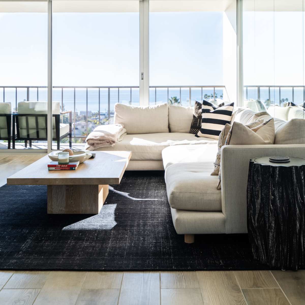 A modern living room with a large sectional sofa, a wooden coffee table, and a view of the ocean through large glass windows.