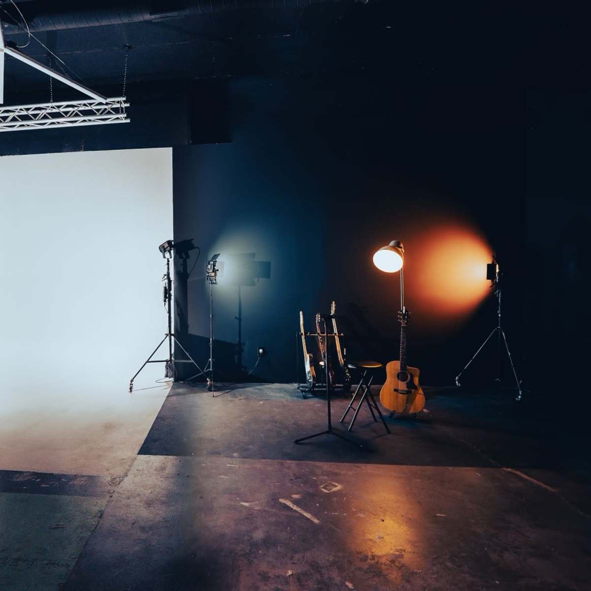 A photography studio with a white backdrop on one side and a dark wall on the other, featuring lighting equipment and a guitar placed on the floor.