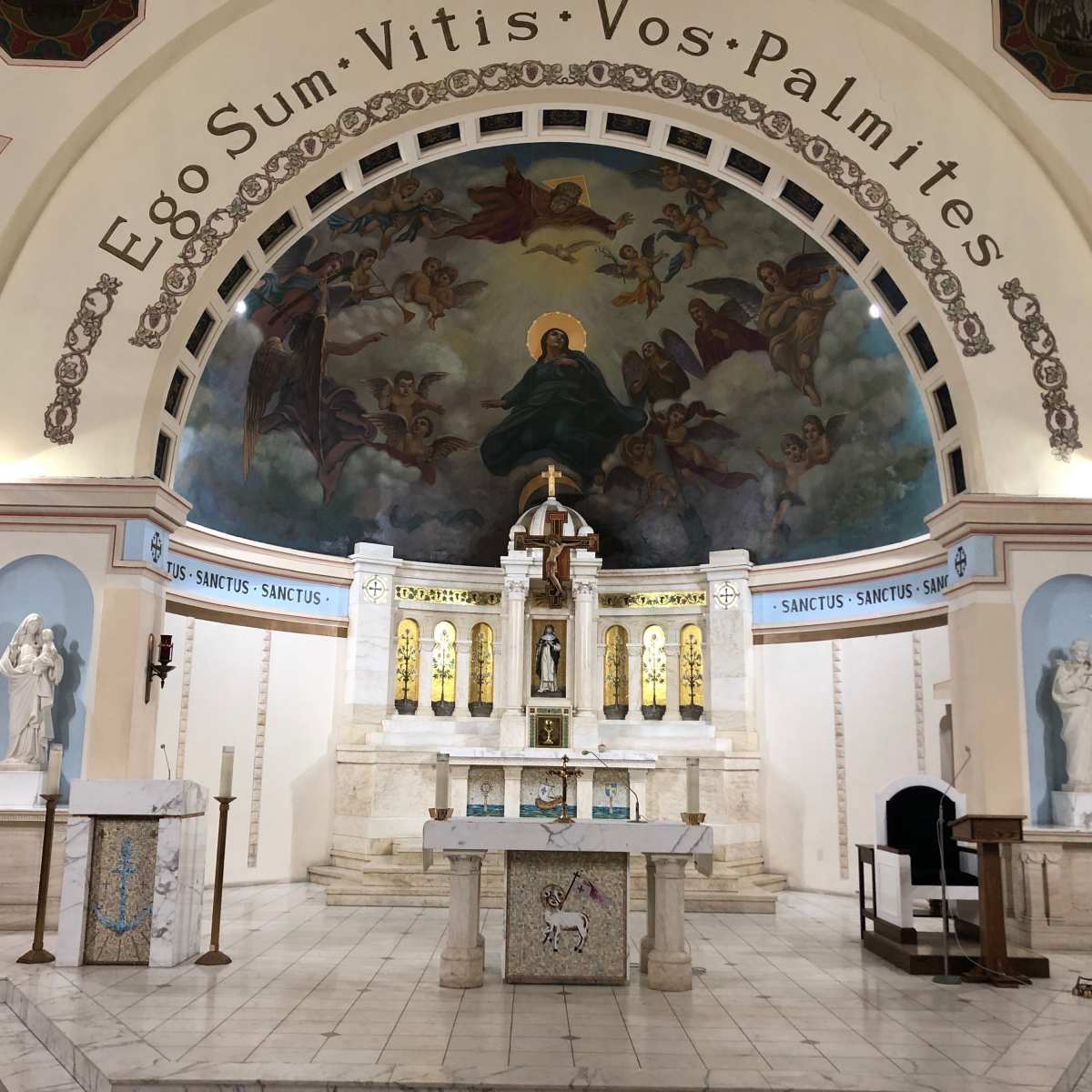 The interior of a church featuring an ornate altar with a large mural above it, surrounded by statues and decorative elements.