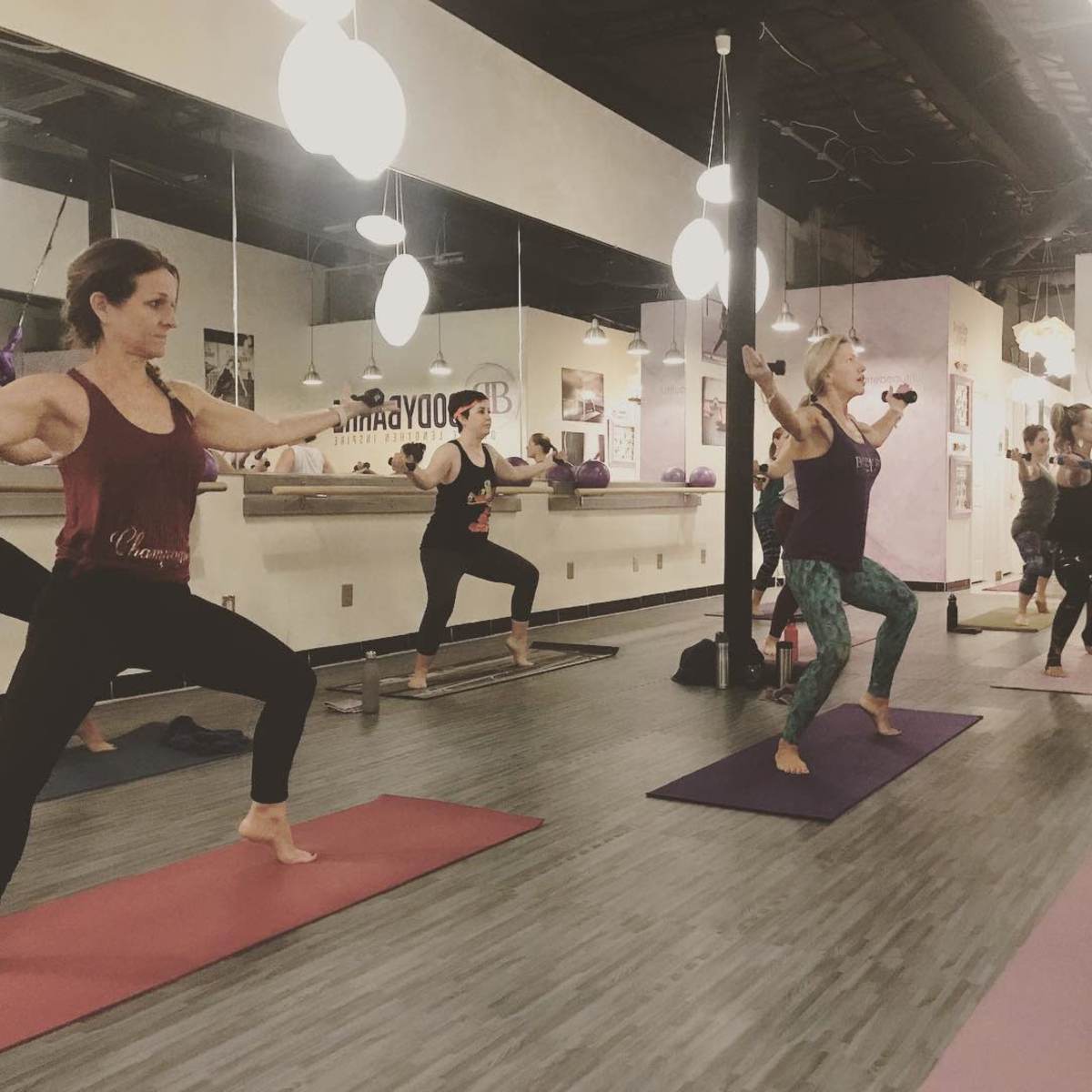 A group of women are performing a workout in a fitness studio with exercise mats and various equipment surrounding them.