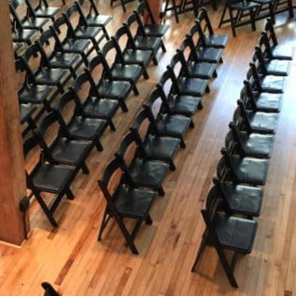 Neatly arranged black folding chairs set up on a wooden floor in a spacious venue.