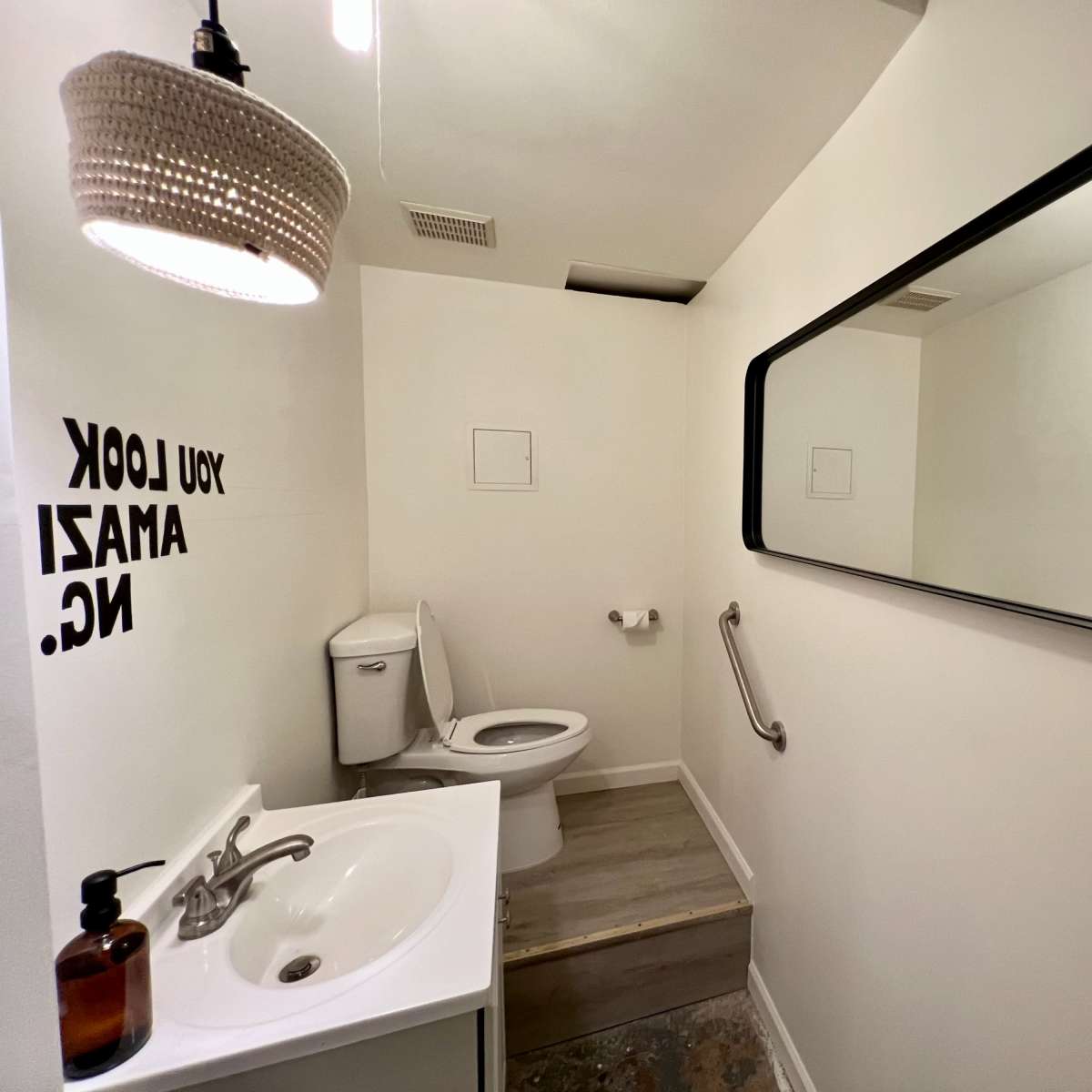 A small bathroom featuring a toilet, a sink with a soap dispenser, and a mirror with motivational text on the walls.
