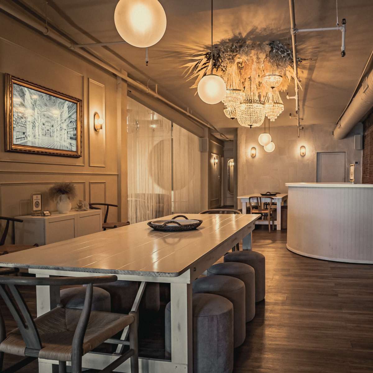 A modern interior space with a long dining table, elegant light fixtures, a decorative ceiling installation, and a bar area, surrounded by exposed brick walls.