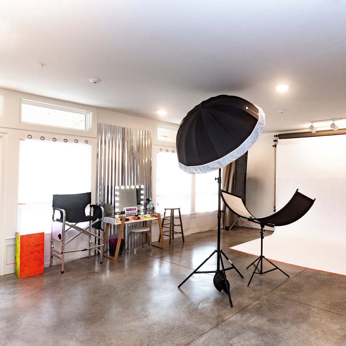 A photography studio featuring a white backdrop, a large umbrella light, and several pieces of equipment arranged around the space.