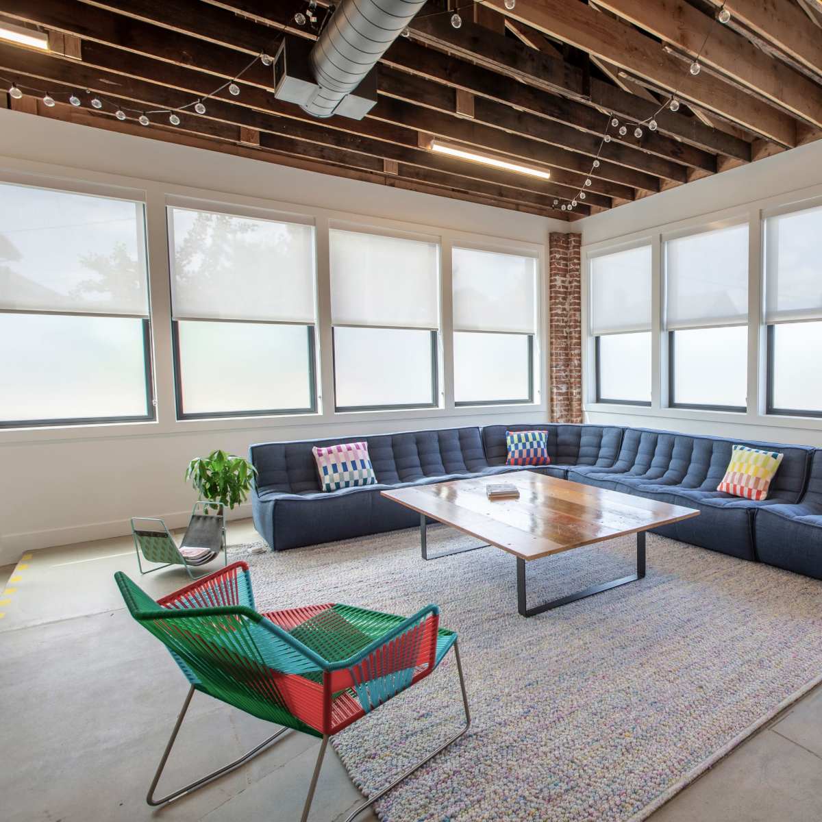 A modern, spacious living room with a large sectional sofa, a wooden coffee table, and several windows allowing natural light to enter.