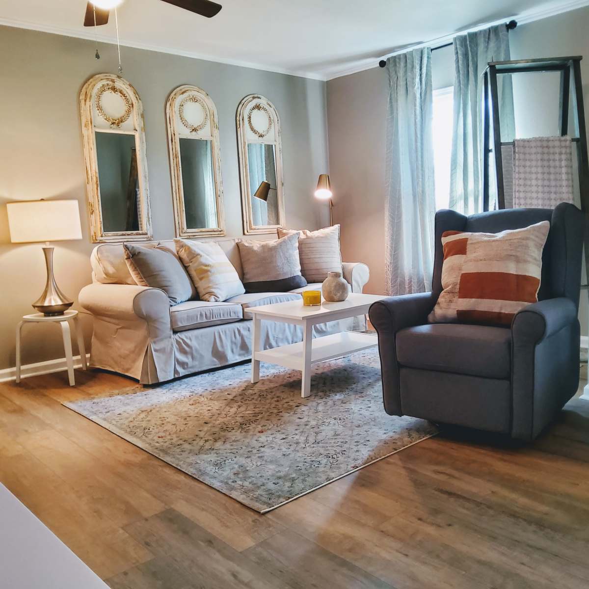 A cozy living room with a white couch, a gray armchair, a small coffee table, and decorative mirrors on the wall.