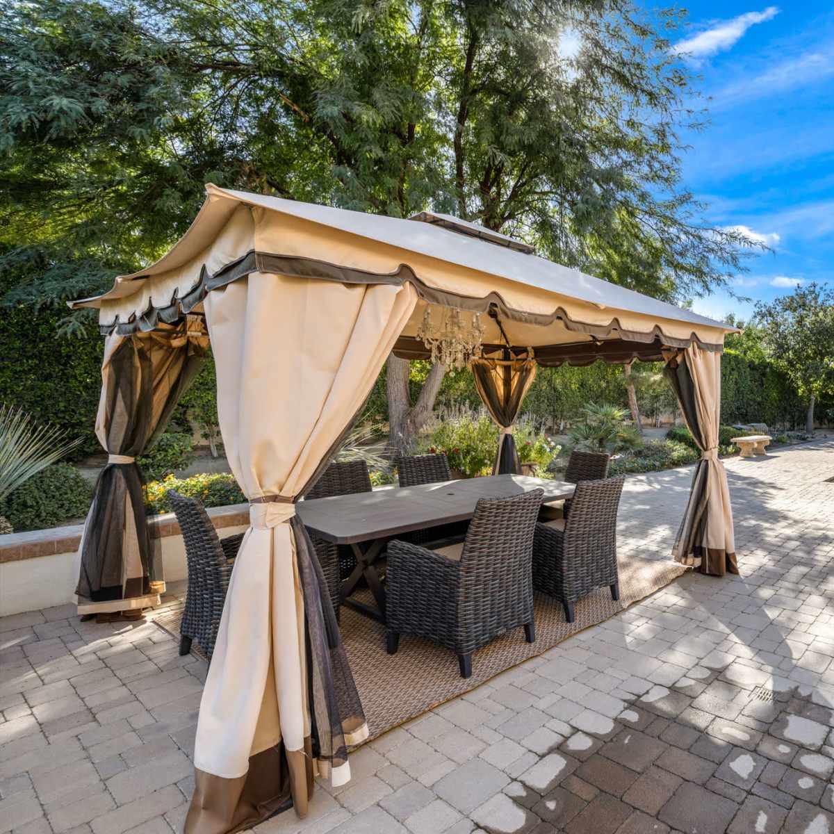 A patio area features a covered gazebo with a dining table and chairs beside a pool surrounded by greenery.