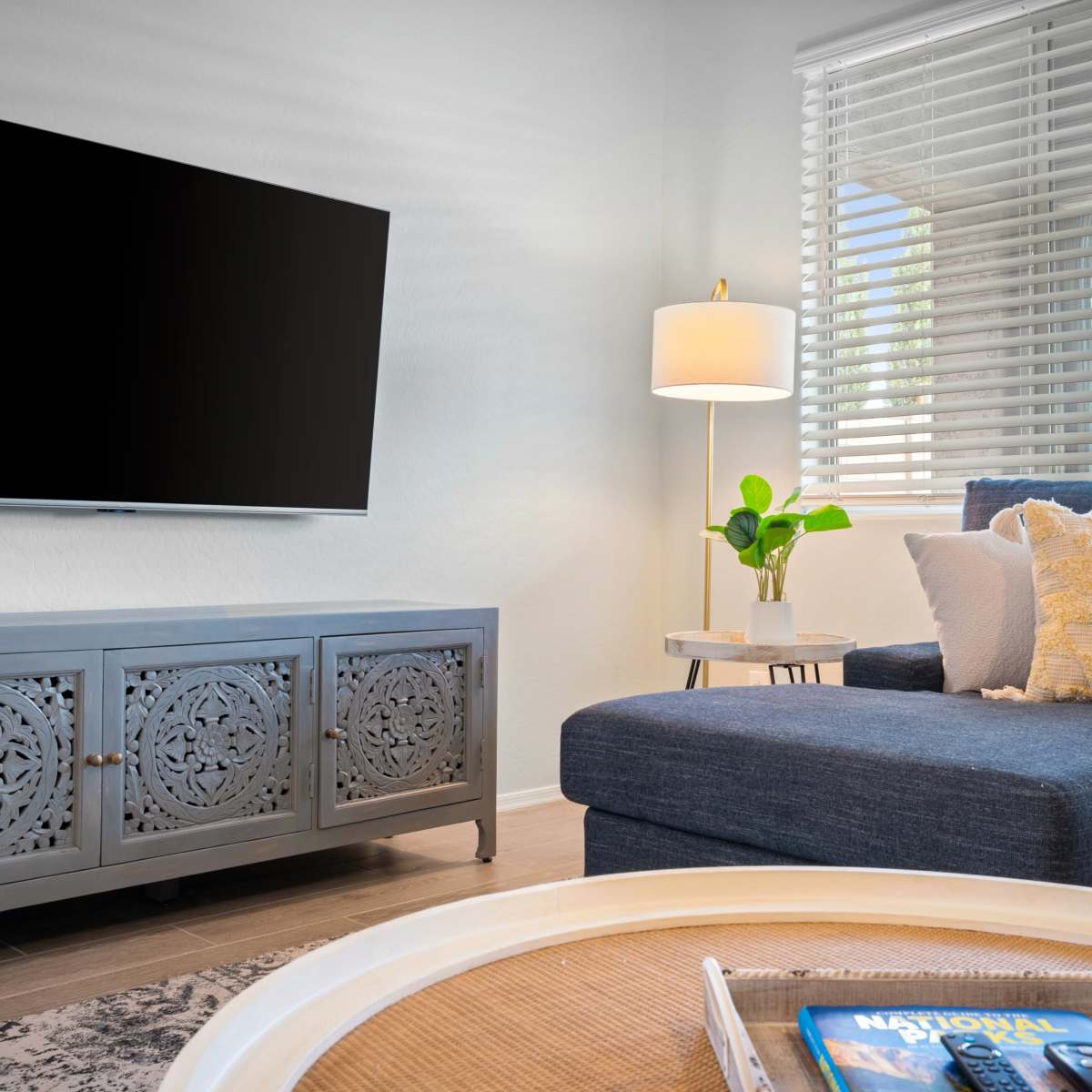 A modern living room features a blue sofa, a decorative cabinet with intricate patterns, a lamp, and a television mounted on the wall.