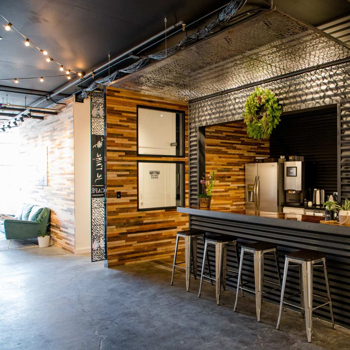 A modern kitchen with a bar area featuring metal stools, a stainless steel refrigerator, and wooden accents on the walls.