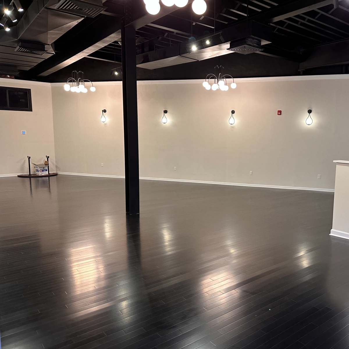 An empty interior space with polished dark wood flooring, white walls, and several light fixtures hanging from the ceiling.