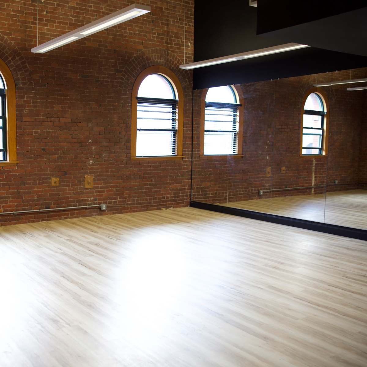 A spacious room with exposed brick walls, large windows, and a mirror along one side.