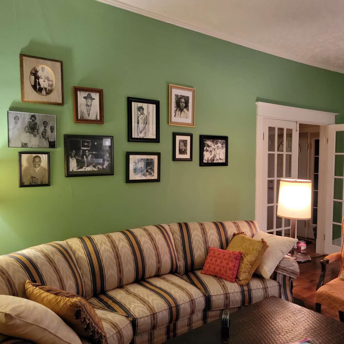 A green living room features a striped sofa, a lamp, and a wall decorated with framed black and white photographs.