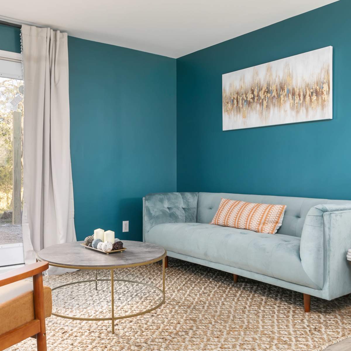 A minimalist living room with a light blue sofa, a round coffee table, and a patterned rug, near a door leading to an outdoor area.