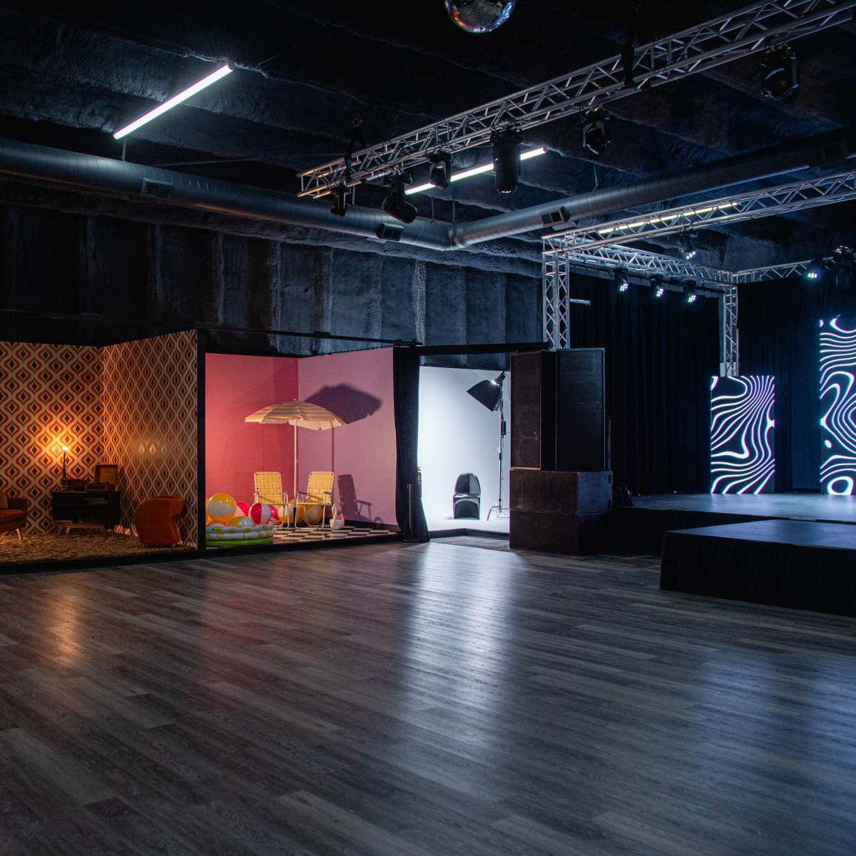 A spacious event space with multiple rooms, each featuring different interior designs, including a swinging chair, a lounge area, and a beach-themed setup.