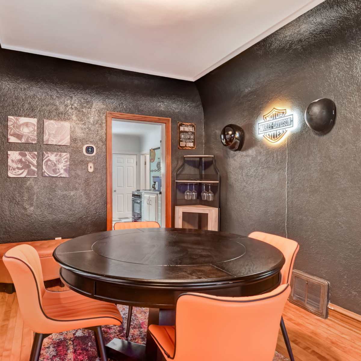A circular black dining table is surrounded by orange chairs in a room with dark walls and a decorative wall hanging.