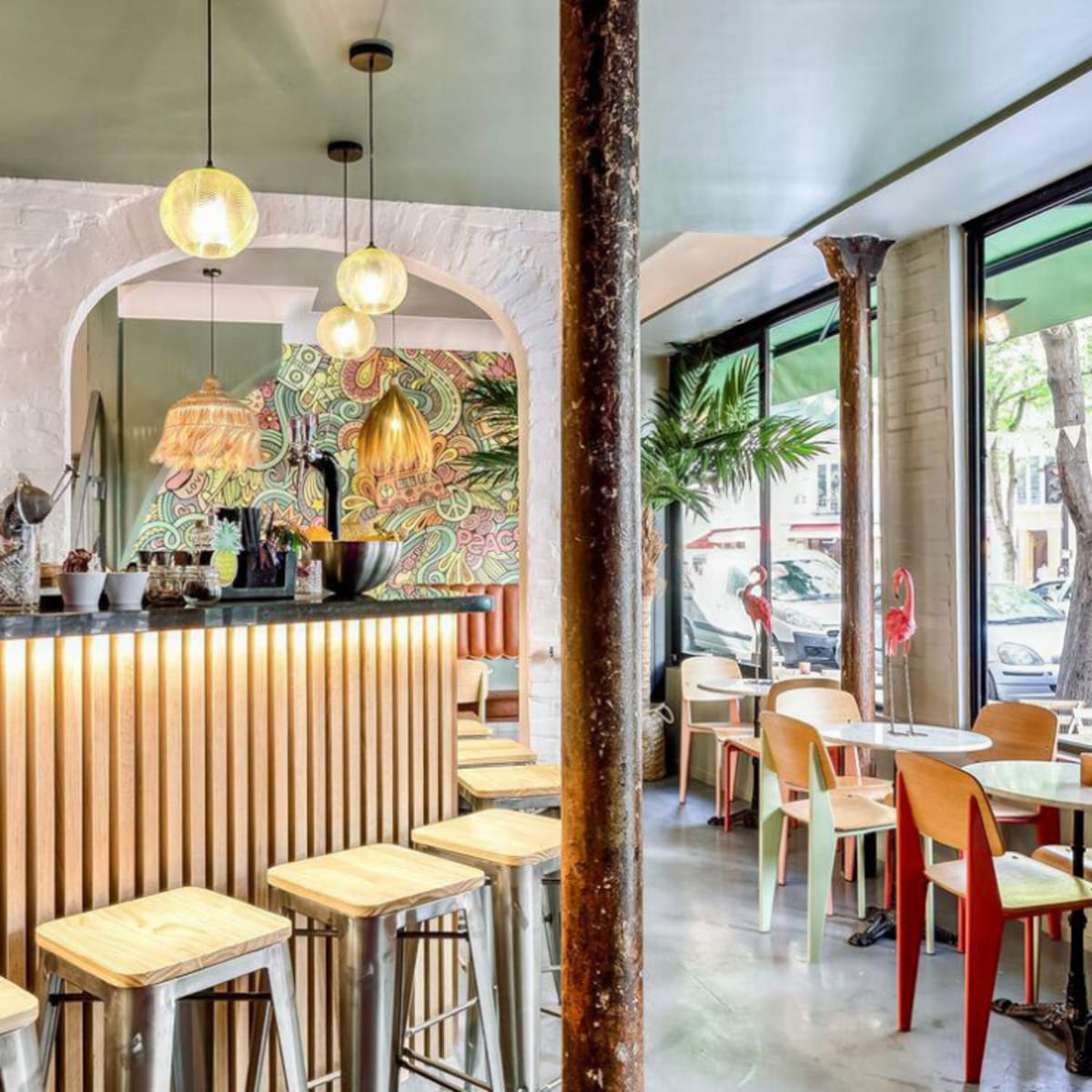 A modern cafe interior featuring a bar with wooden accents, several round tables, and large windows letting in natural light.
