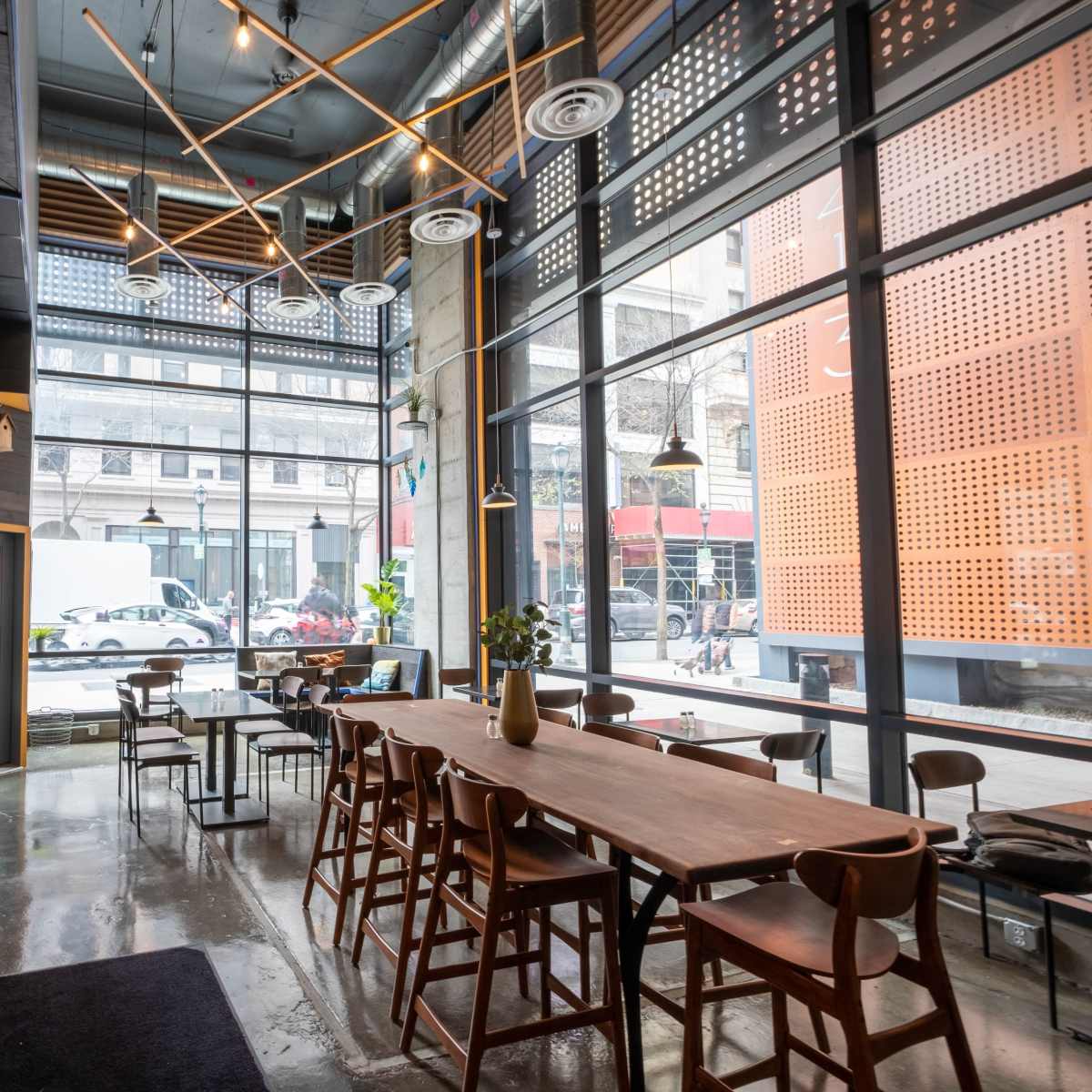 A modern cafe interior featuring wooden tables, chairs, and large windows with a view of the street outside.