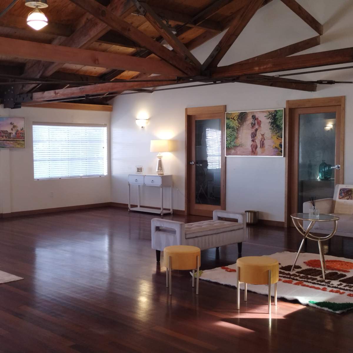 A spacious room with wooden beams, hardwood flooring, and a seating arrangement that includes a small table and chairs, along with decorative artwork on the walls.