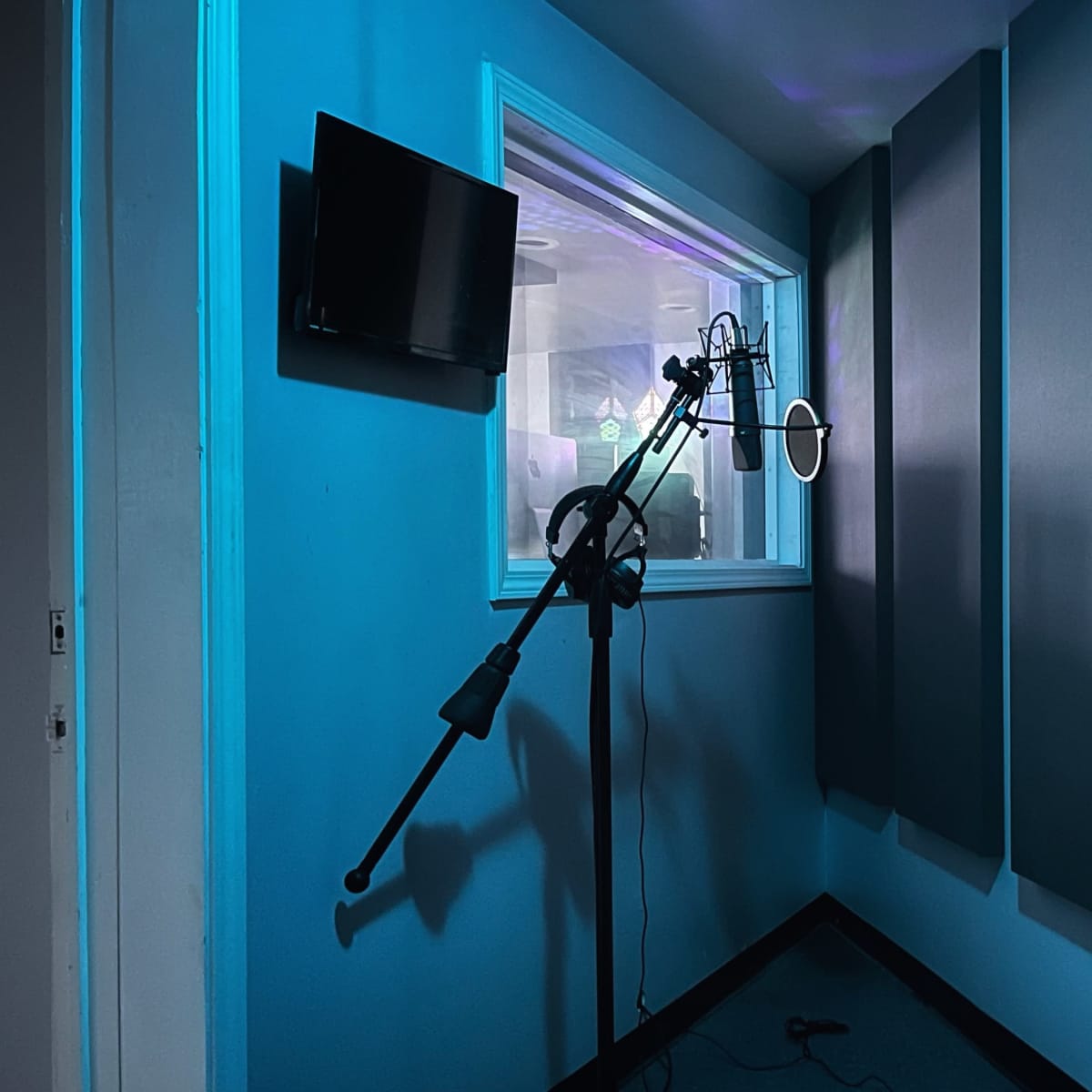 A soundproof recording studio with a microphone on a stand and a circular light near a glass window.