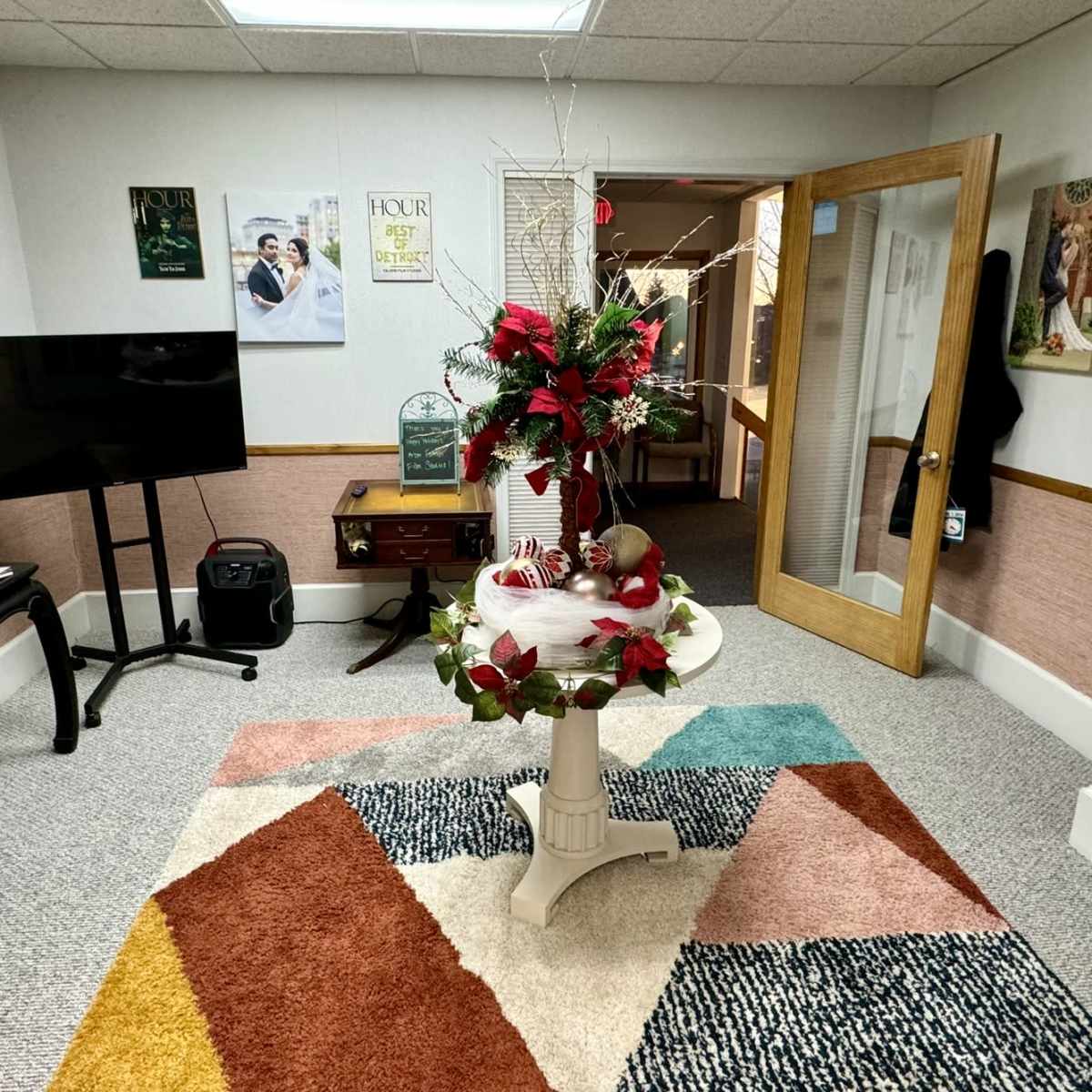 A small room with a colorful rug, a round table decorated with flowers, a television, and various wall decorations.