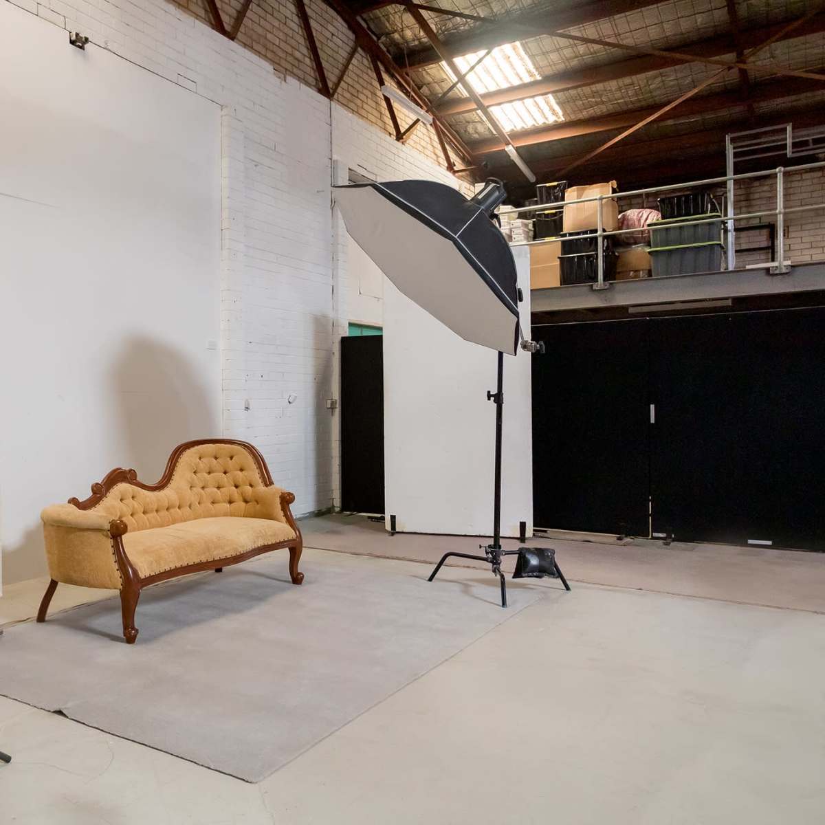 A photography studio setup featuring a vintage sofa on a rug, with two lighting fixtures and a plain backdrop.