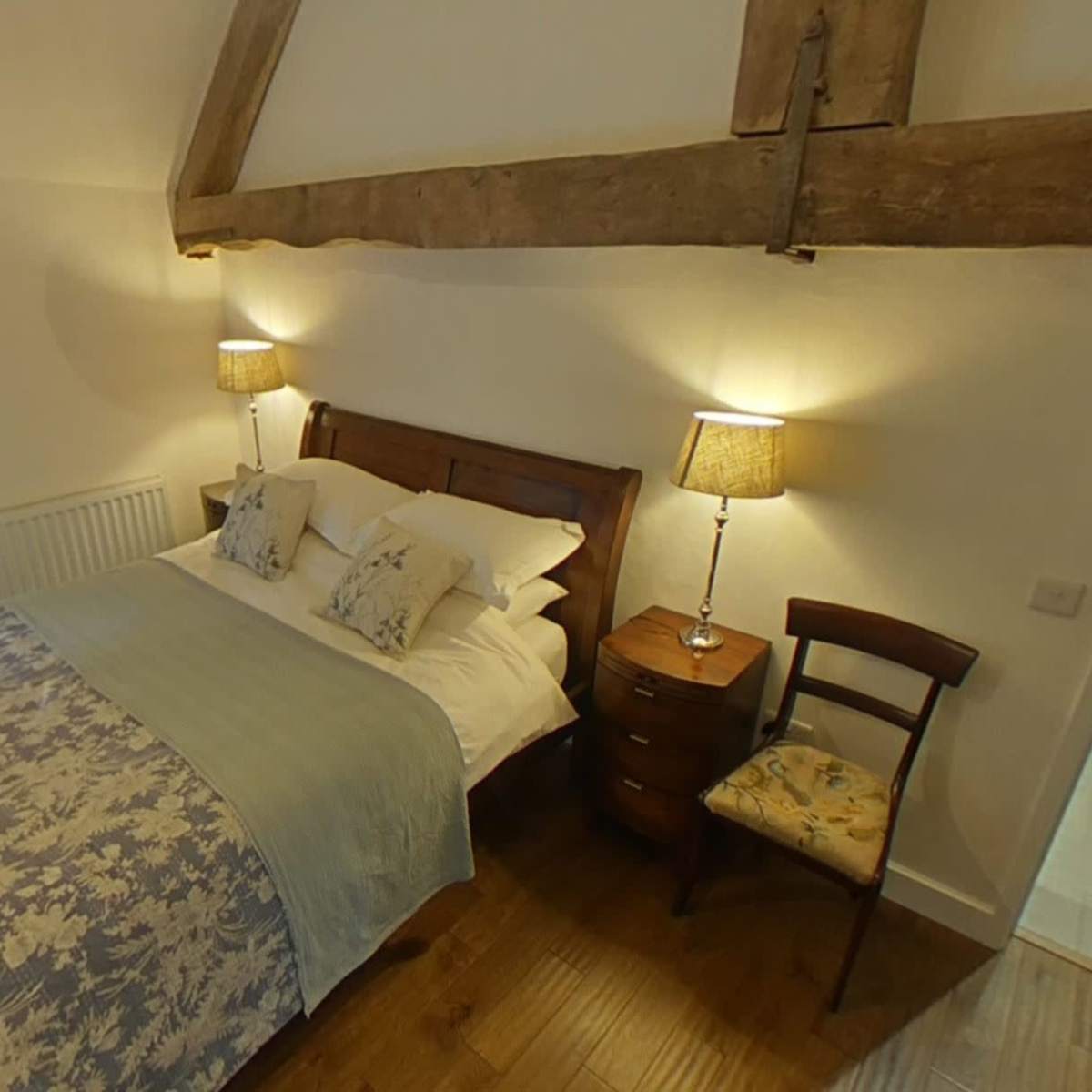 A cozy bedroom featuring a wooden bed, bedside lamps, a chair, and an en-suite bathroom.