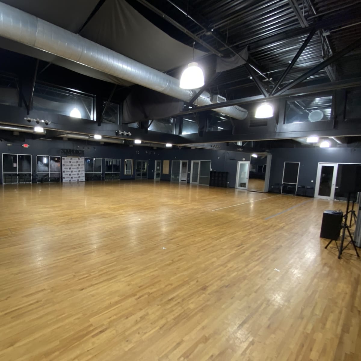 A spacious dance studio with a smooth wooden floor, large windows, and dim lighting.