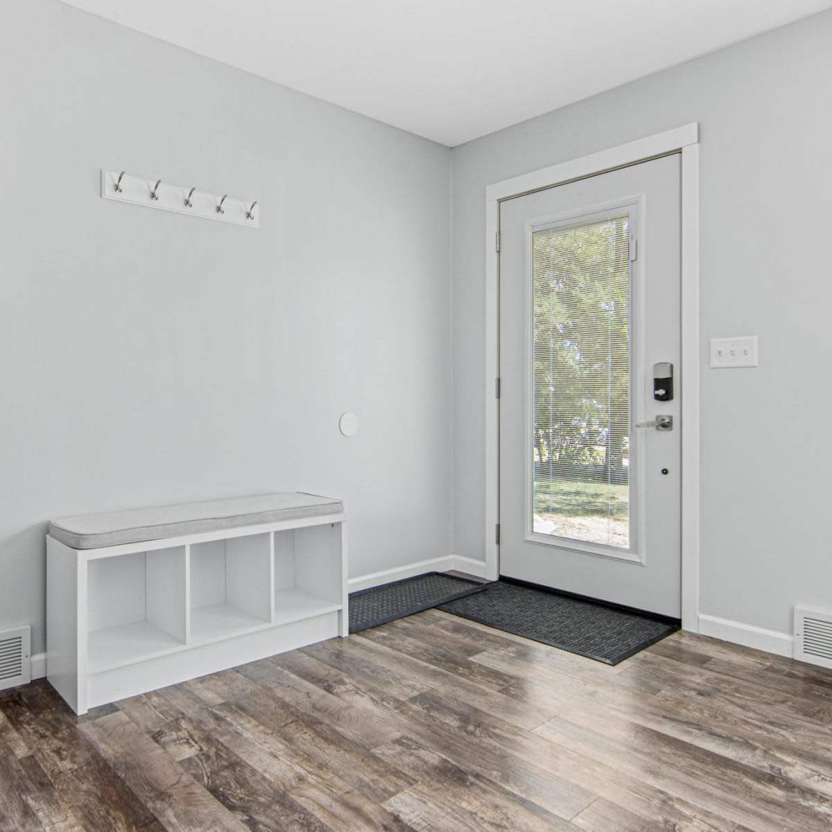 A minimalist entryway with a bench, coat hooks, a mirror, and a door leading outside.