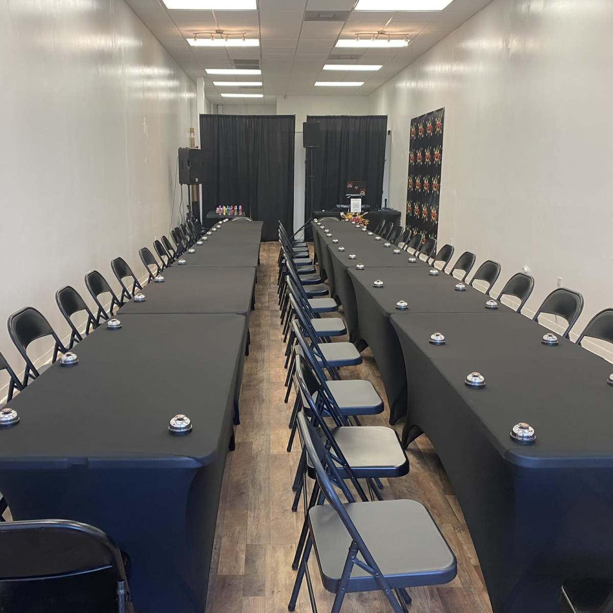 A rectangular conference room setup with two long tables covered in black cloth, facing each other with chairs arranged along both sides.