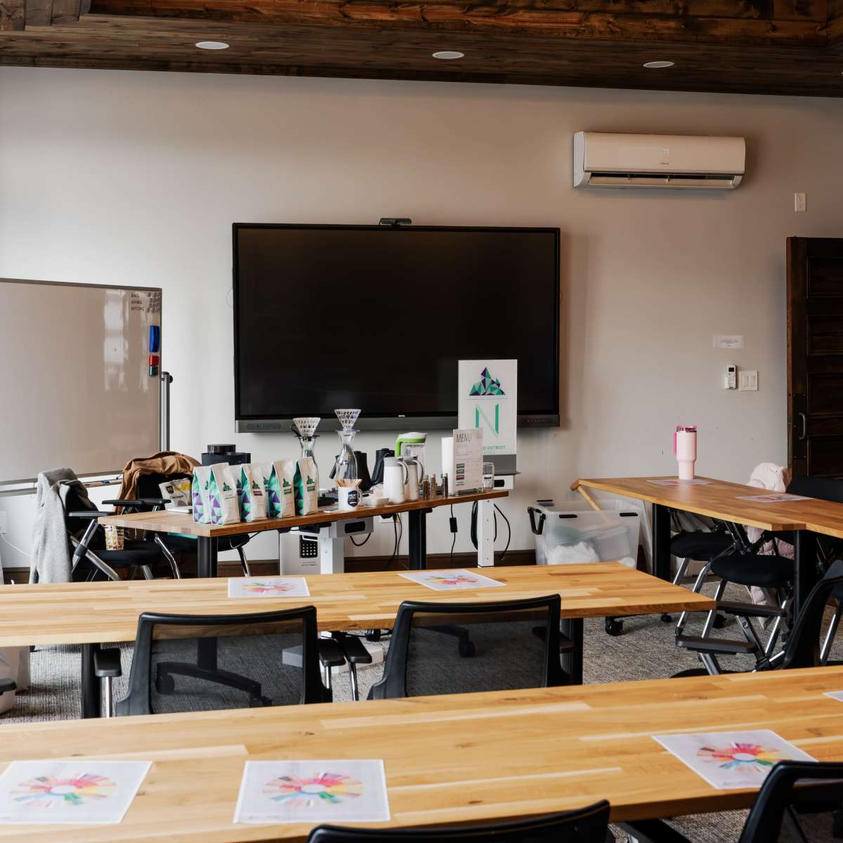 A spacious room with wooden tables and chairs, equipped with a large screen and various presentation materials on a side table.