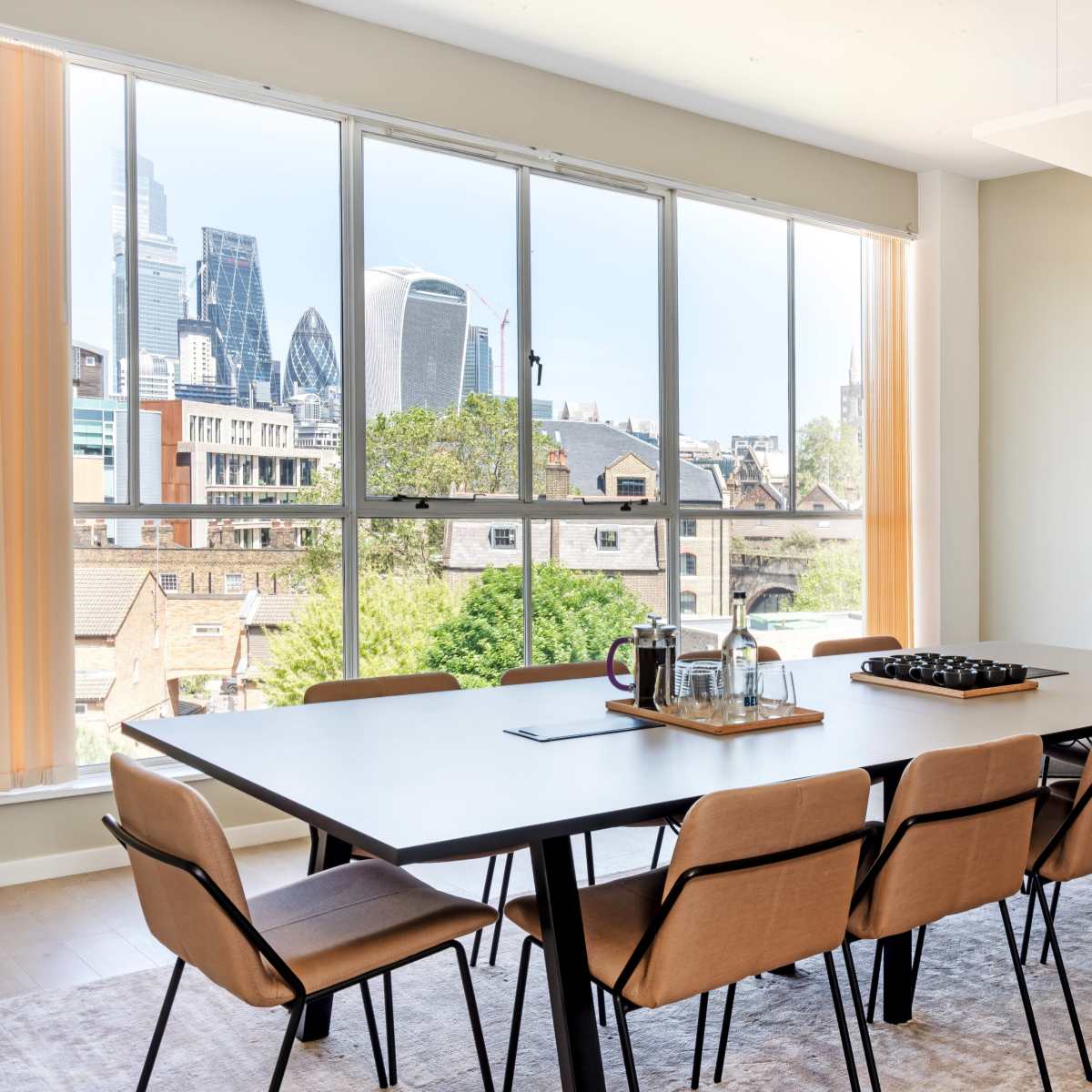 A modern conference room features a large table surrounded by chairs, with floor-to-ceiling windows showing a city skyline.