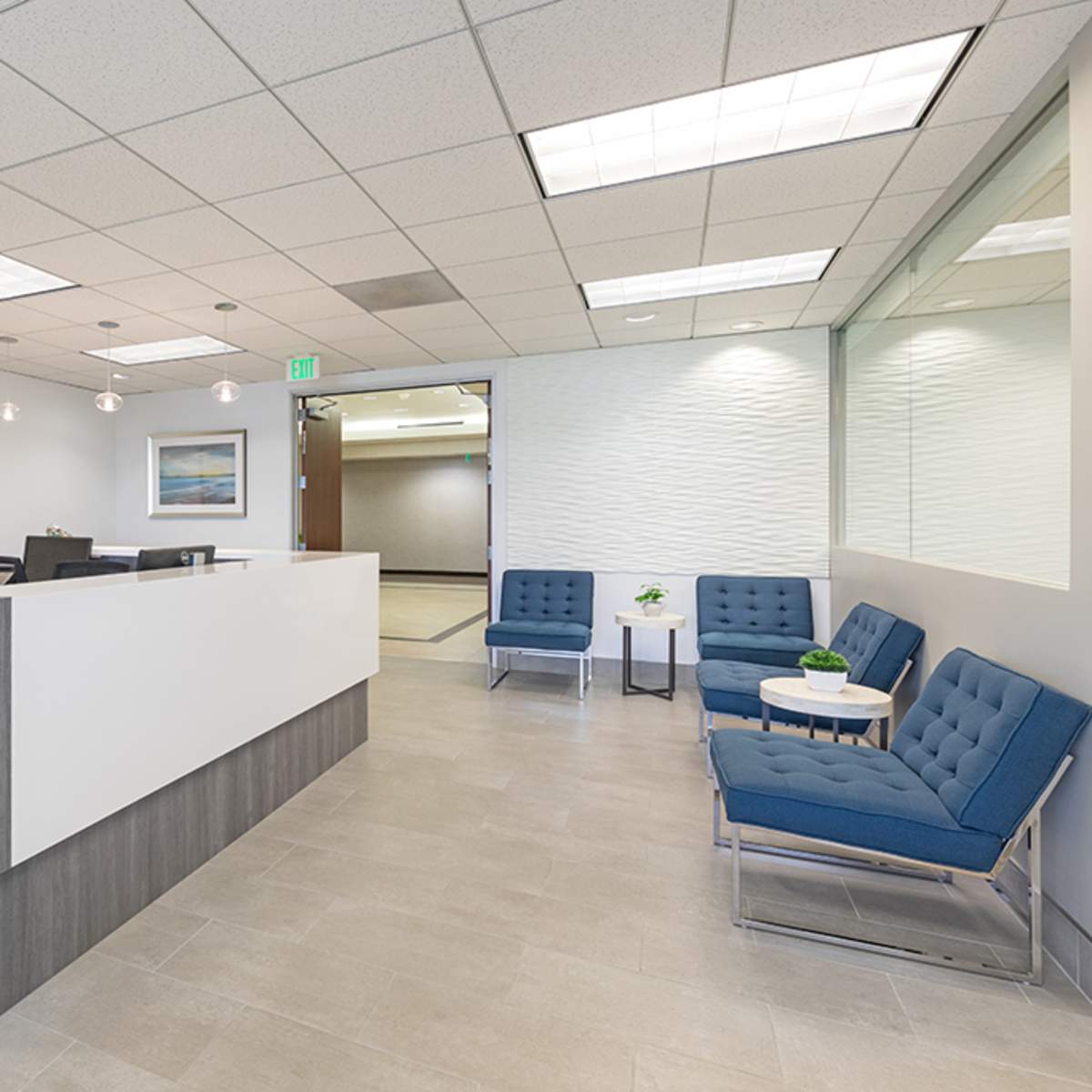 A modern reception area with a gray front desk, blue seating along the wall, and abstract artwork on the walls.