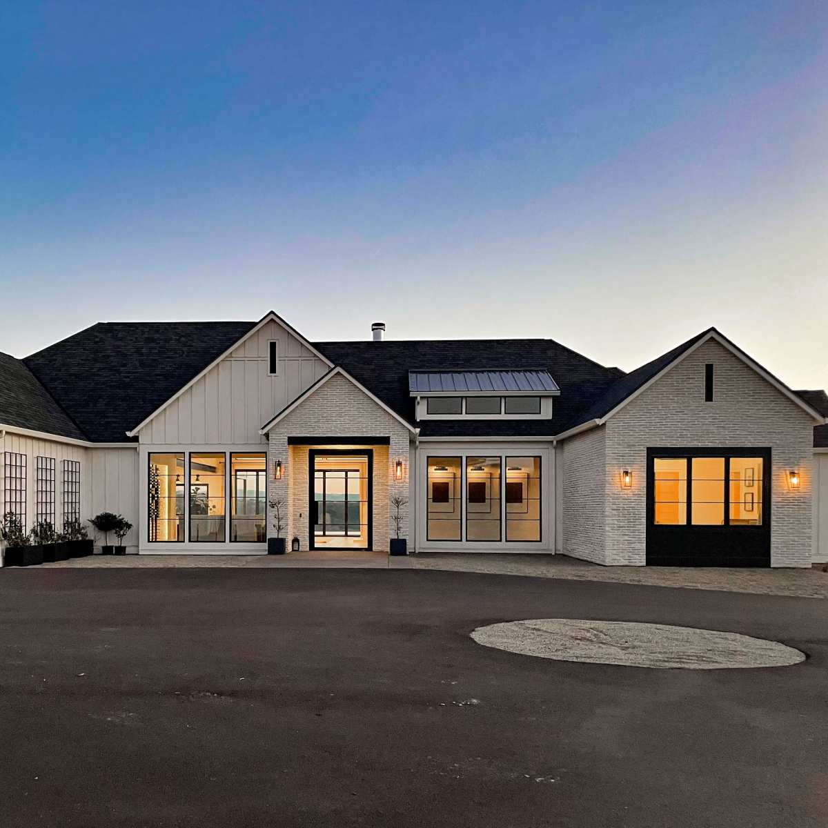 A modern single-story house features a combination of white siding and stone, with large windows and a three-car garage.