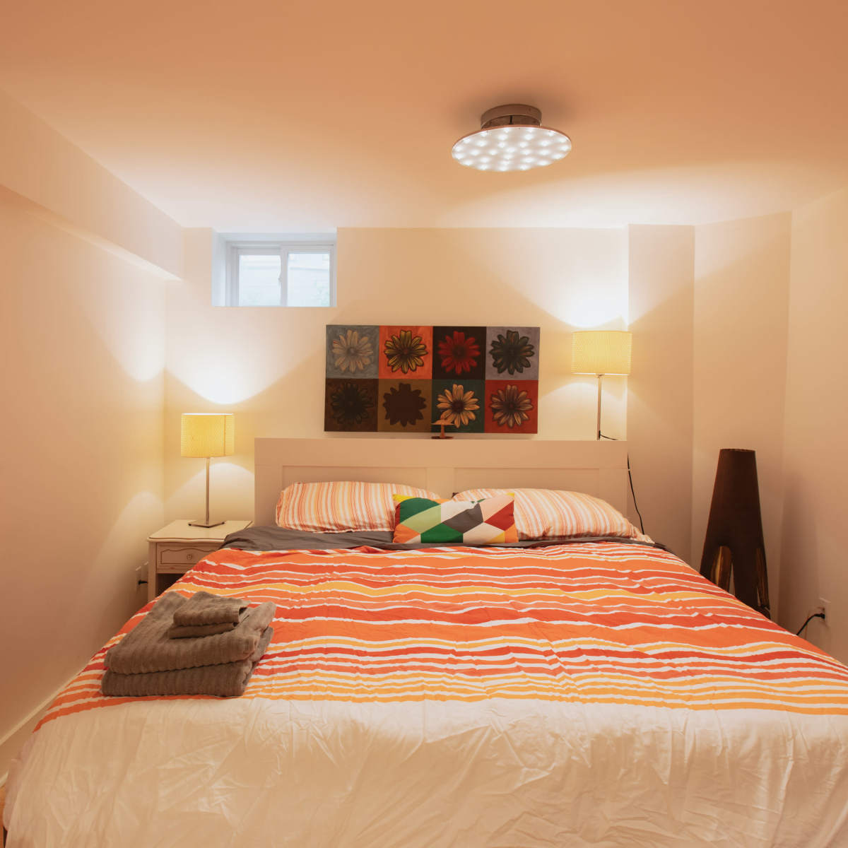 A furnished bedroom featuring a striped bedspread, a tall lamp, and a wall decoration with flower patterns.