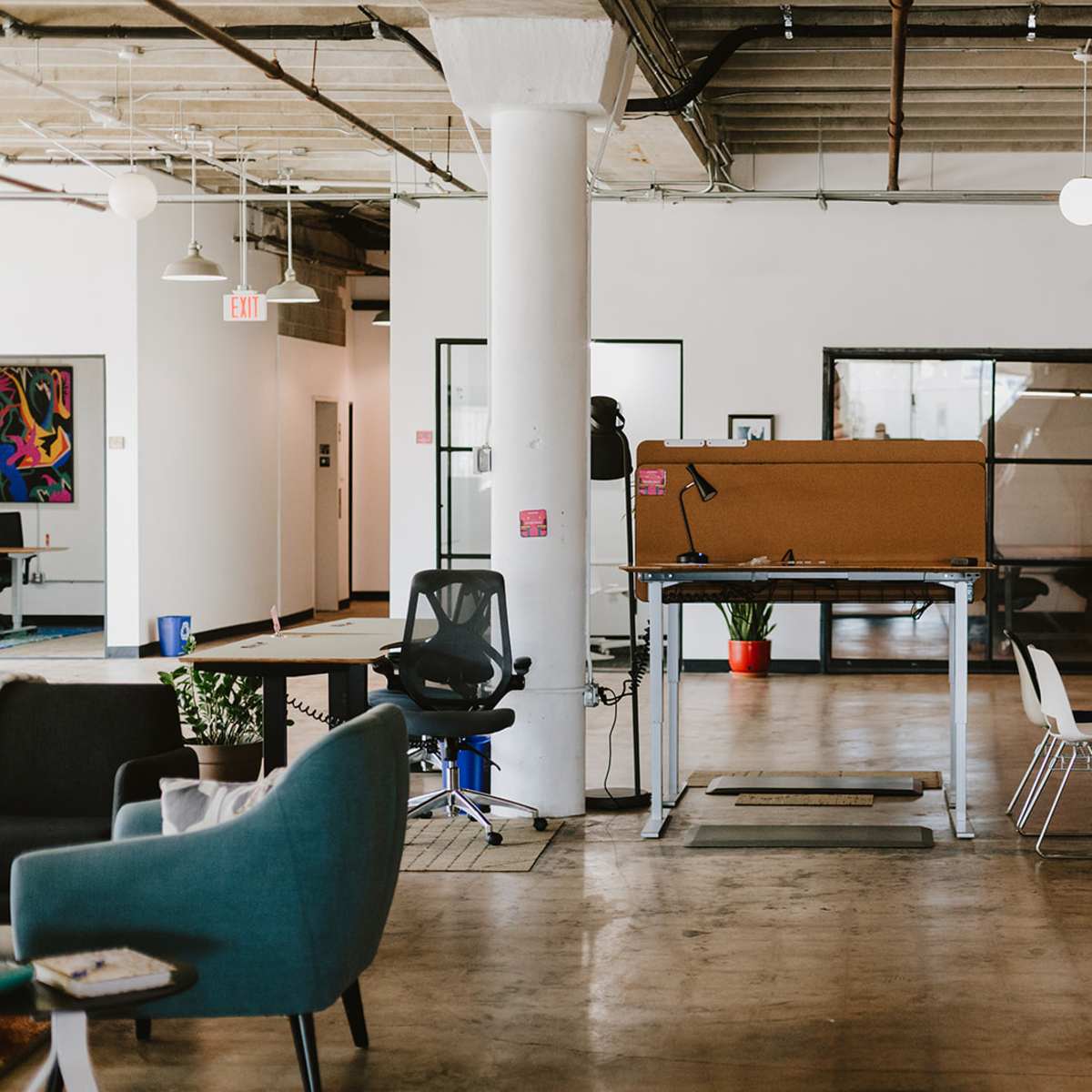 A spacious office interior with a standing desk in the center, surrounded by open seating areas and glass conference rooms.