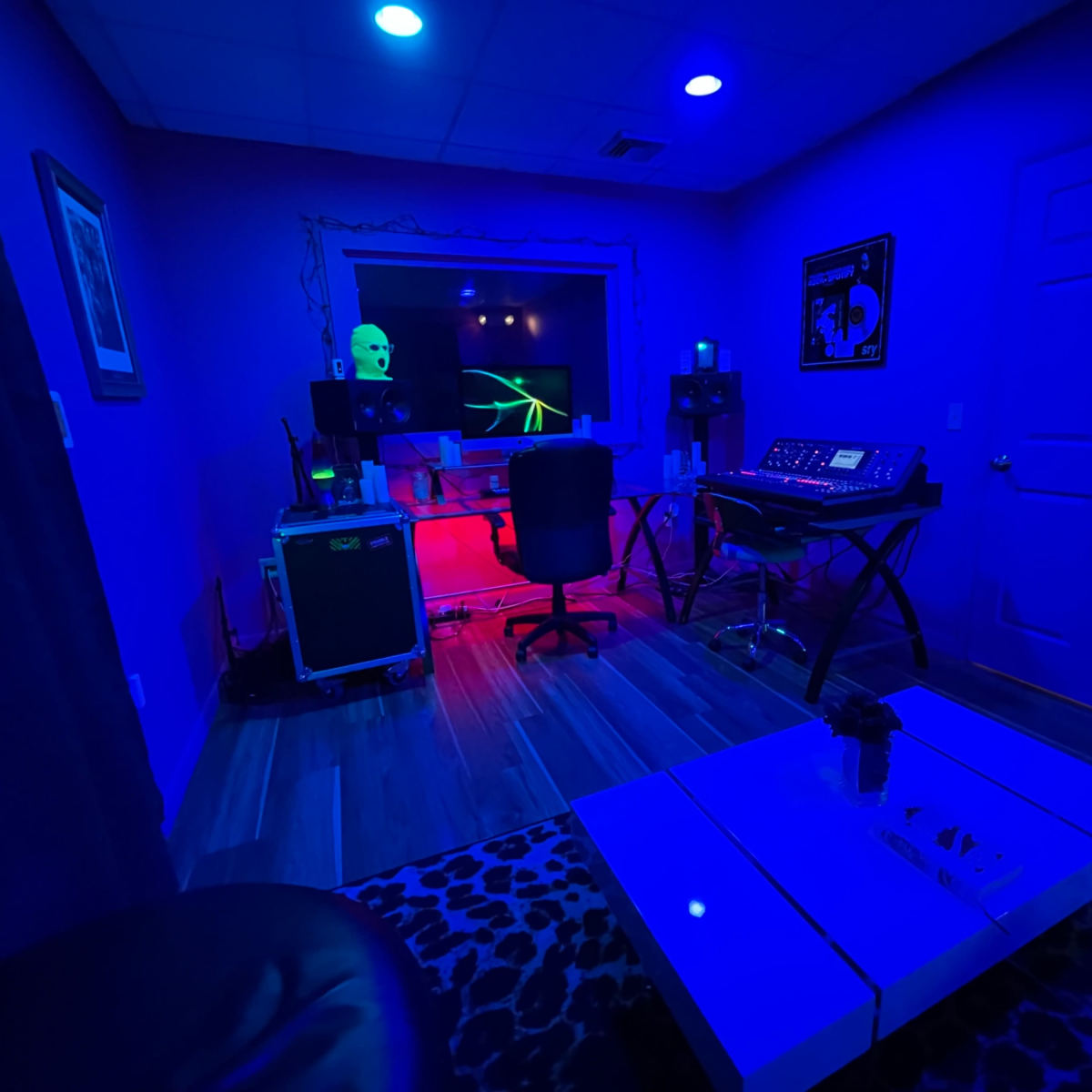 A dimly lit music studio featuring a desk with equipment, a chair, and colorful lighting effects.