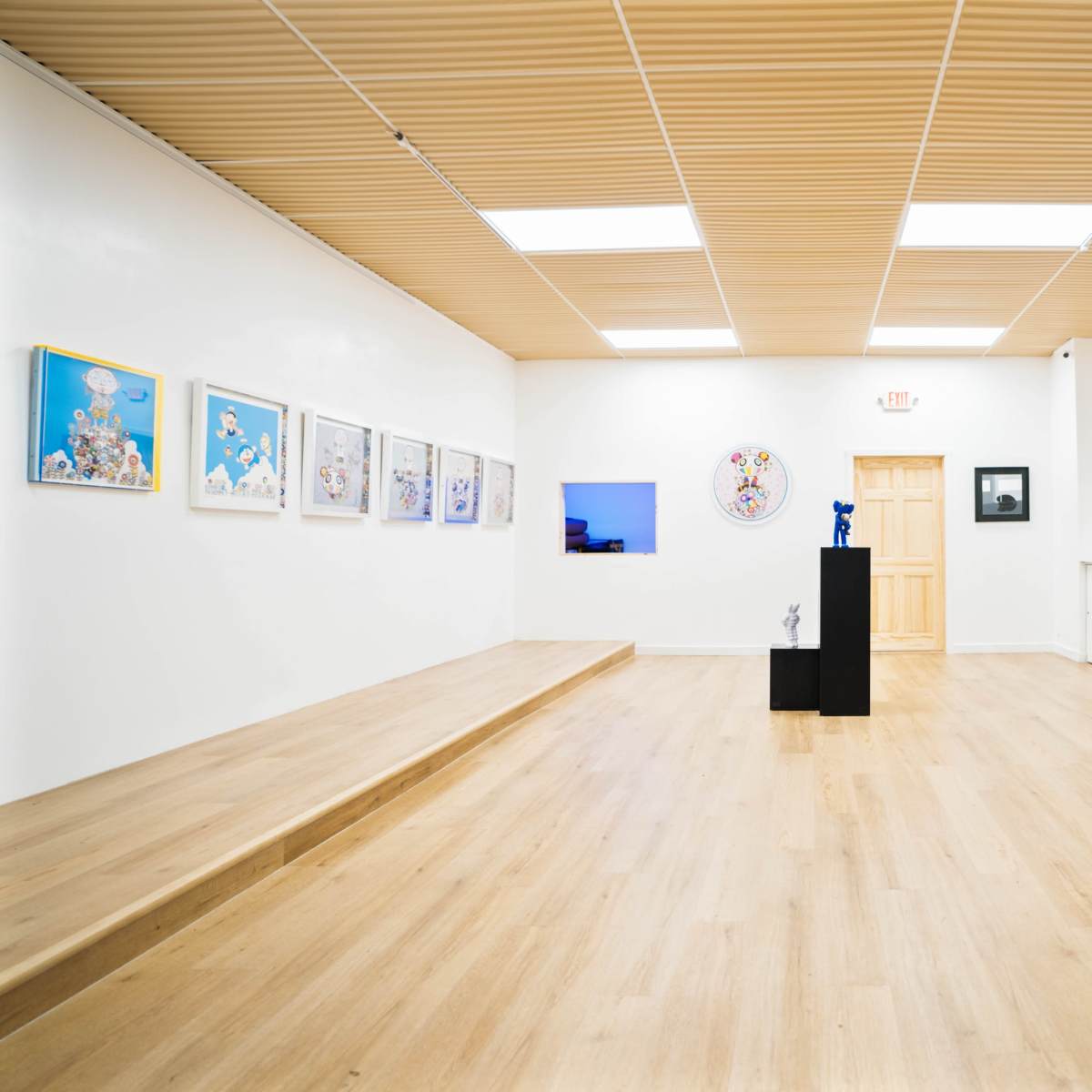 An art gallery featuring an array of framed artworks on the white walls and a central black pedestal displaying a sculpture.