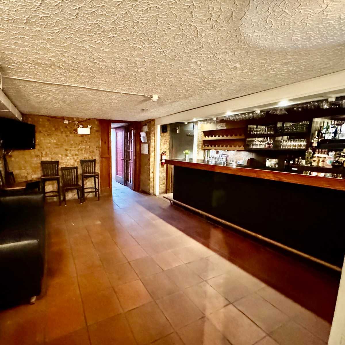A spacious bar area with a dark countertop, several chairs, and a doorway leading outside.