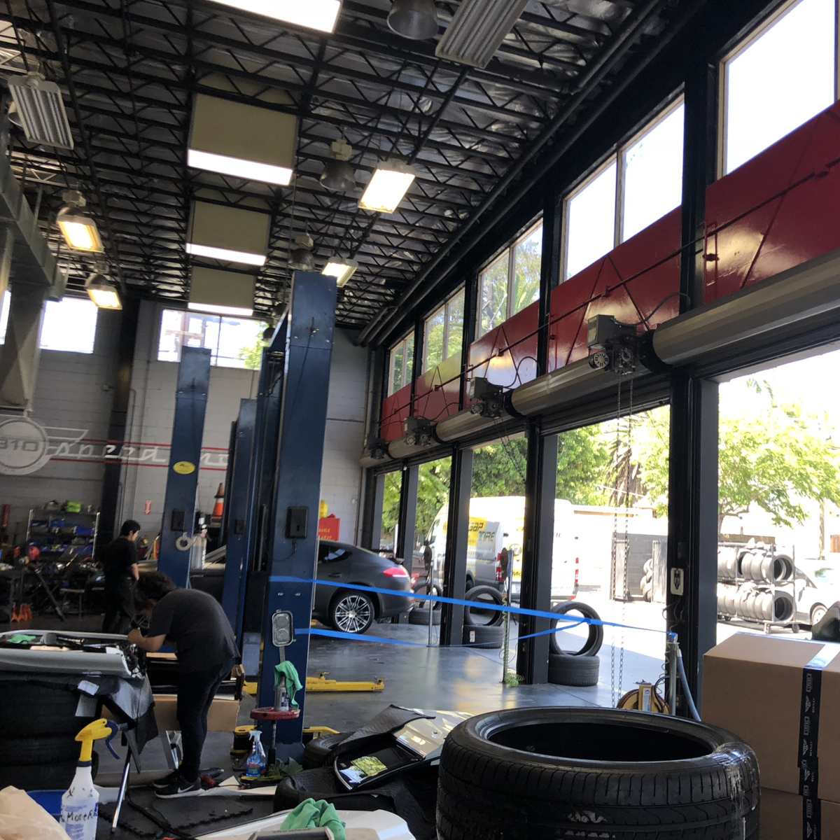 An auto repair shop with large windows, displaying tires and equipment, and workers engaged in various tasks.