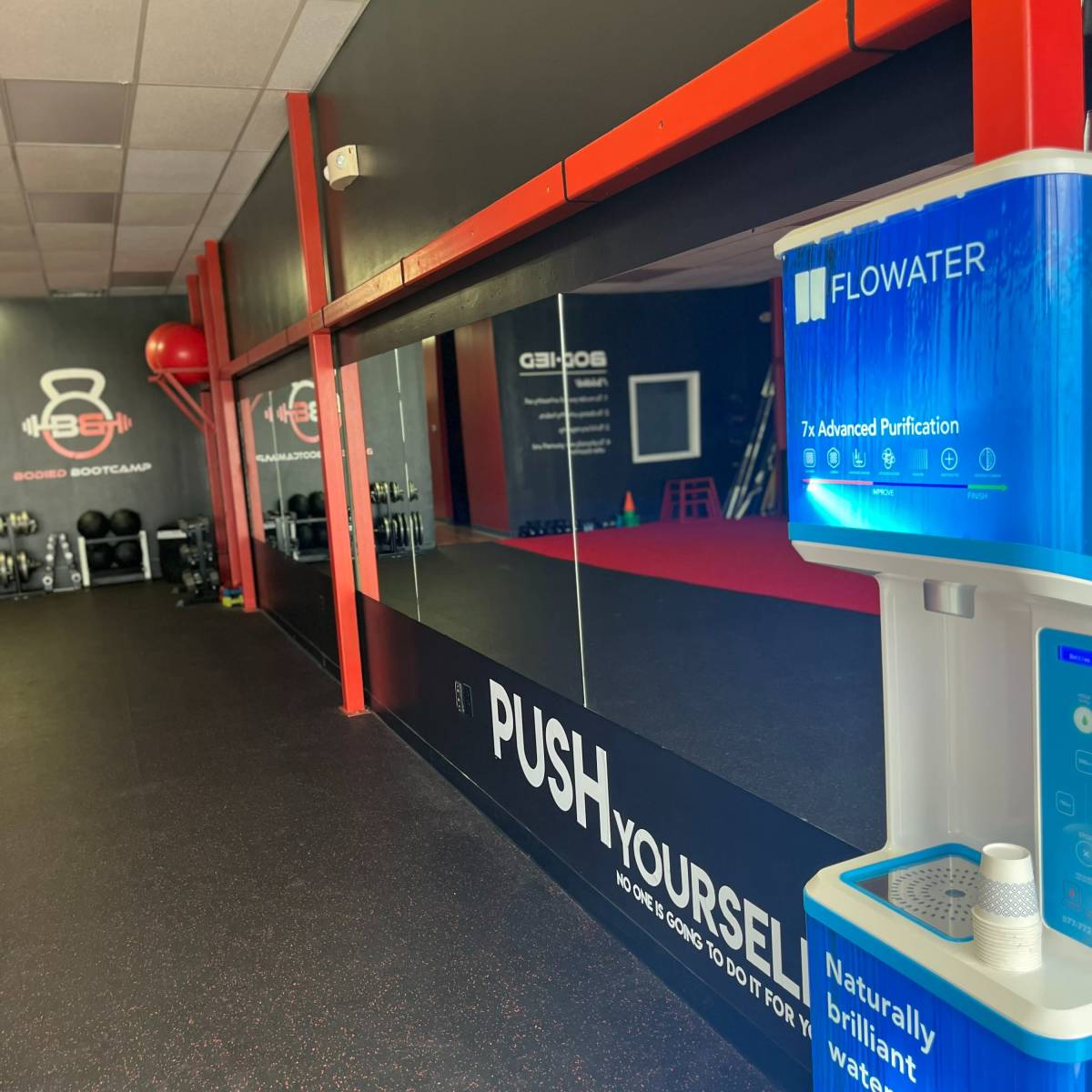 The interior of a gym with a large mirror, a water refill station, and motivational text on the wall.