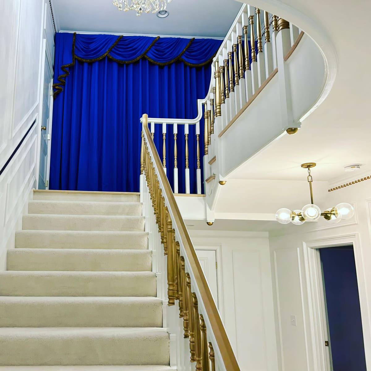 A staircase leading to a landing with a blue curtain and a chandelier above.