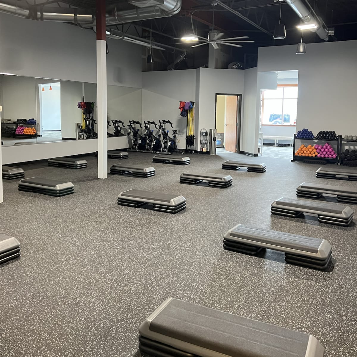 An empty gym space featuring multiple workout benches arranged in rows, with exercise equipment and weights visible in the background.