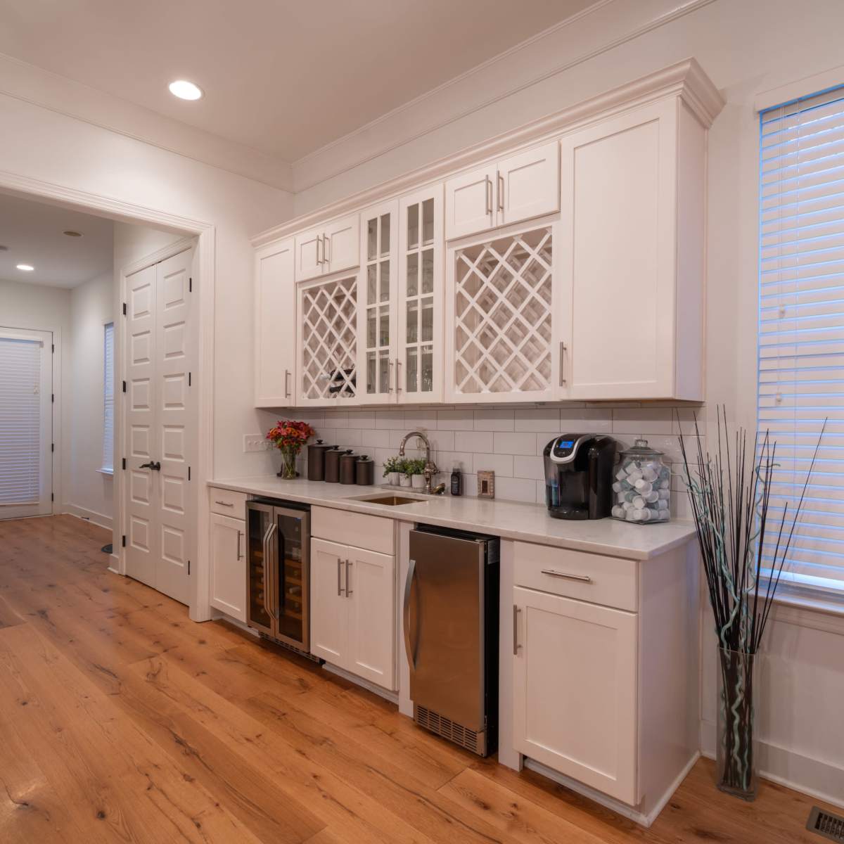 A modern kitchen with white cabinetry, a wine cooler, and a doorway leading to a hallway.