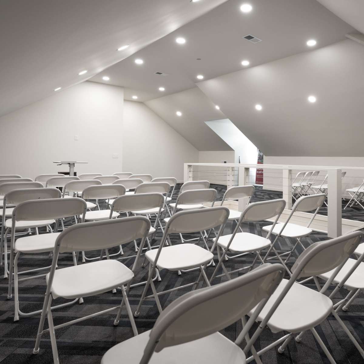 A spacious attic room with white folding chairs arranged in rows and bright ceiling lights illuminating the space.