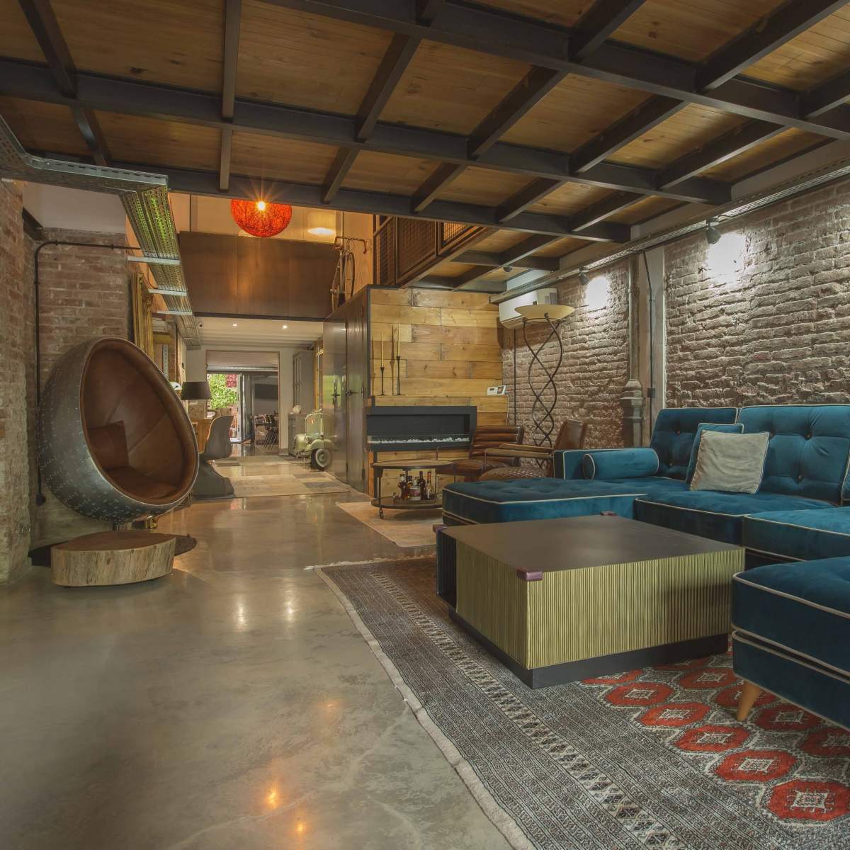 A modern living room with a blue sectional couch, a round chair, and exposed brick walls.
